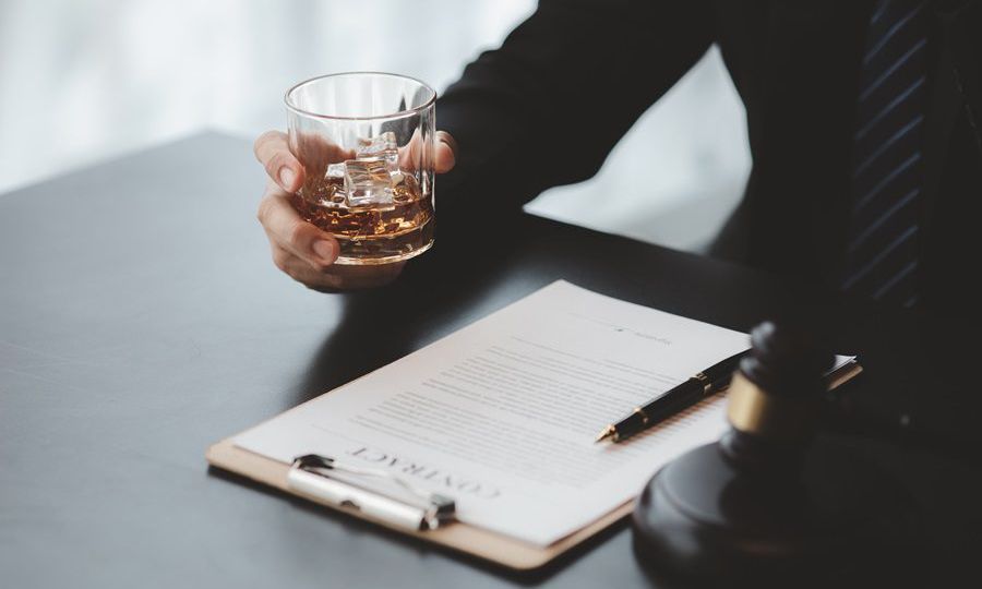 A lawyer holding a glass of whiskey, He's in his office, and he'