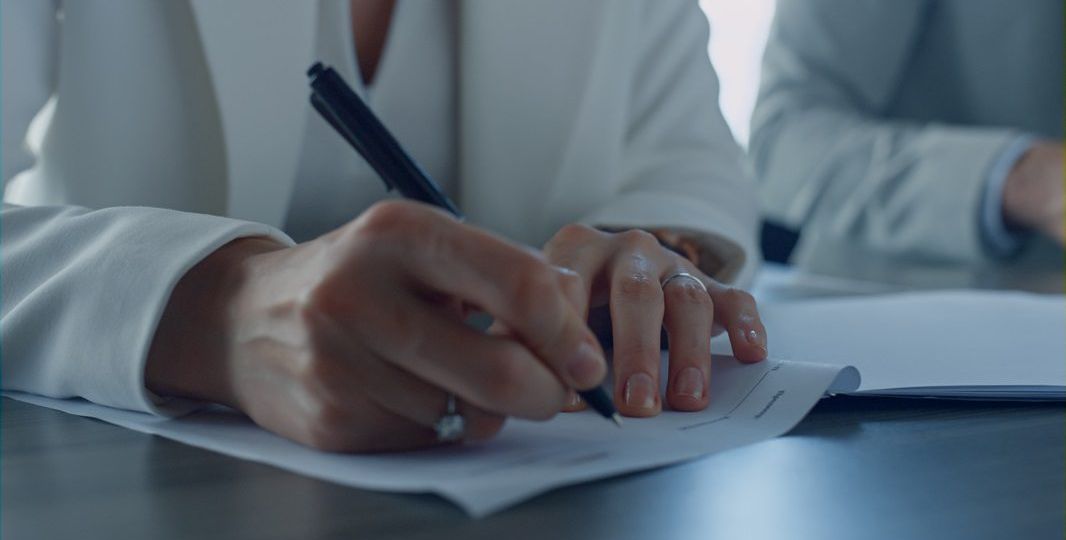 Closeup hand holding pen. Divorcing woman signing documents in attorney office.